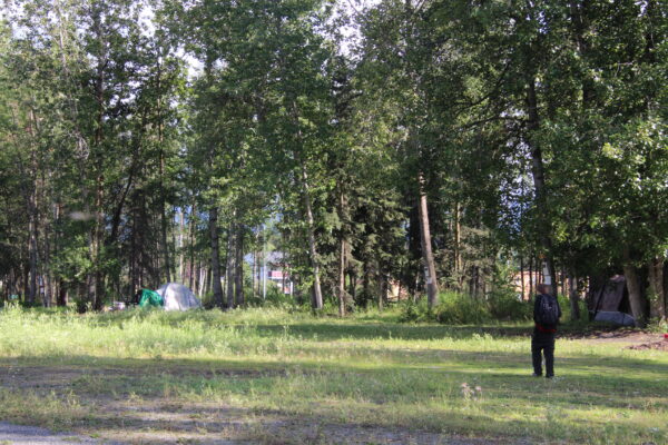 A man in black walks towards a tent in some trees