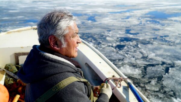 A man wearing a jacket in a boat looks out over sea ice.