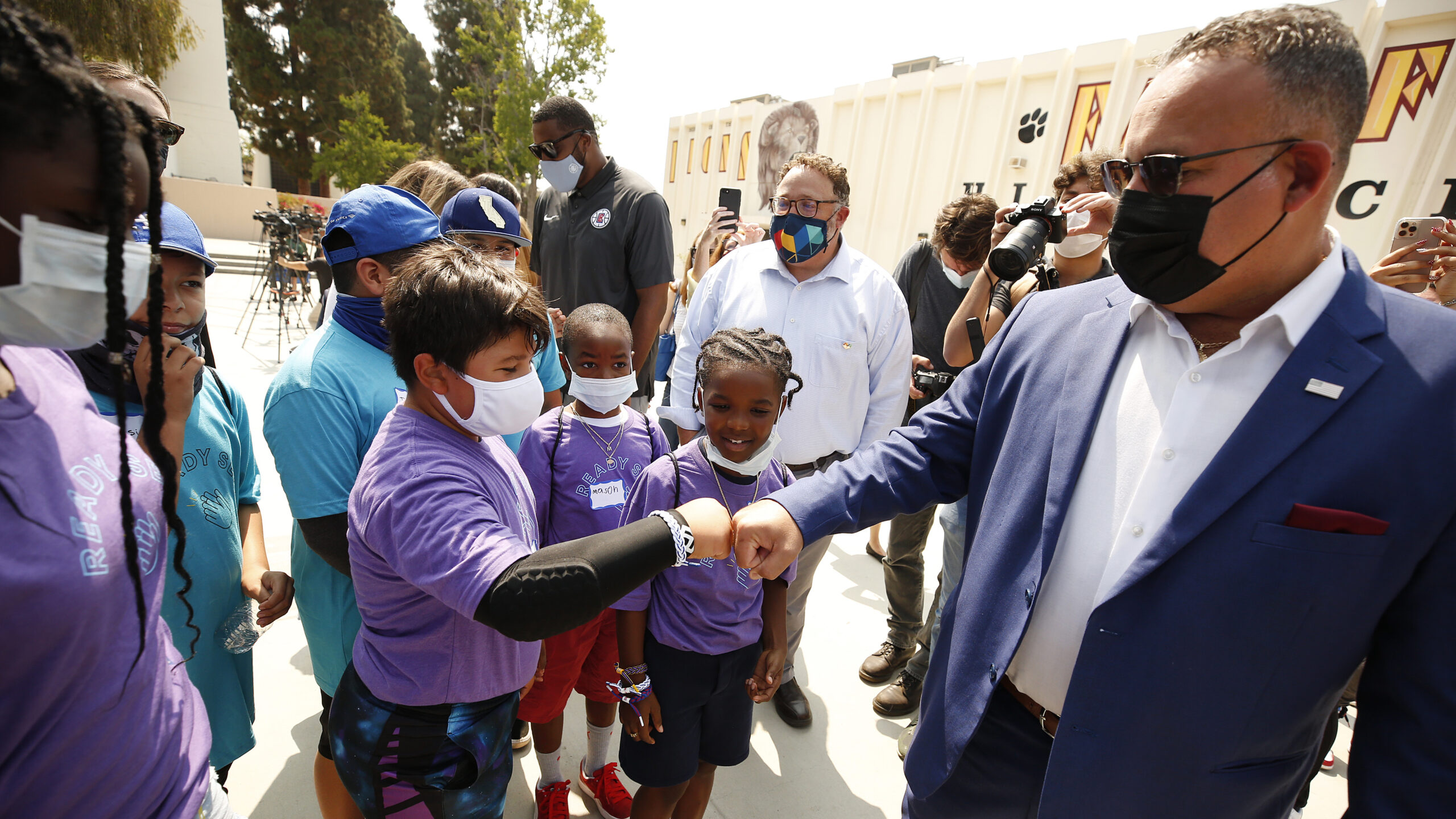 A man in a face mask fist bumps a child who is also wearing a face mask.
