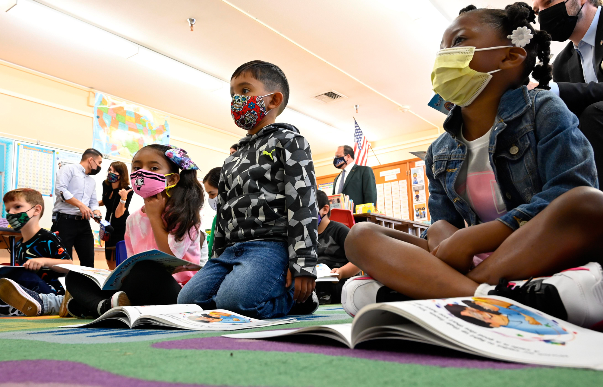 Students sit on the carpet wearing face masks and reading books.