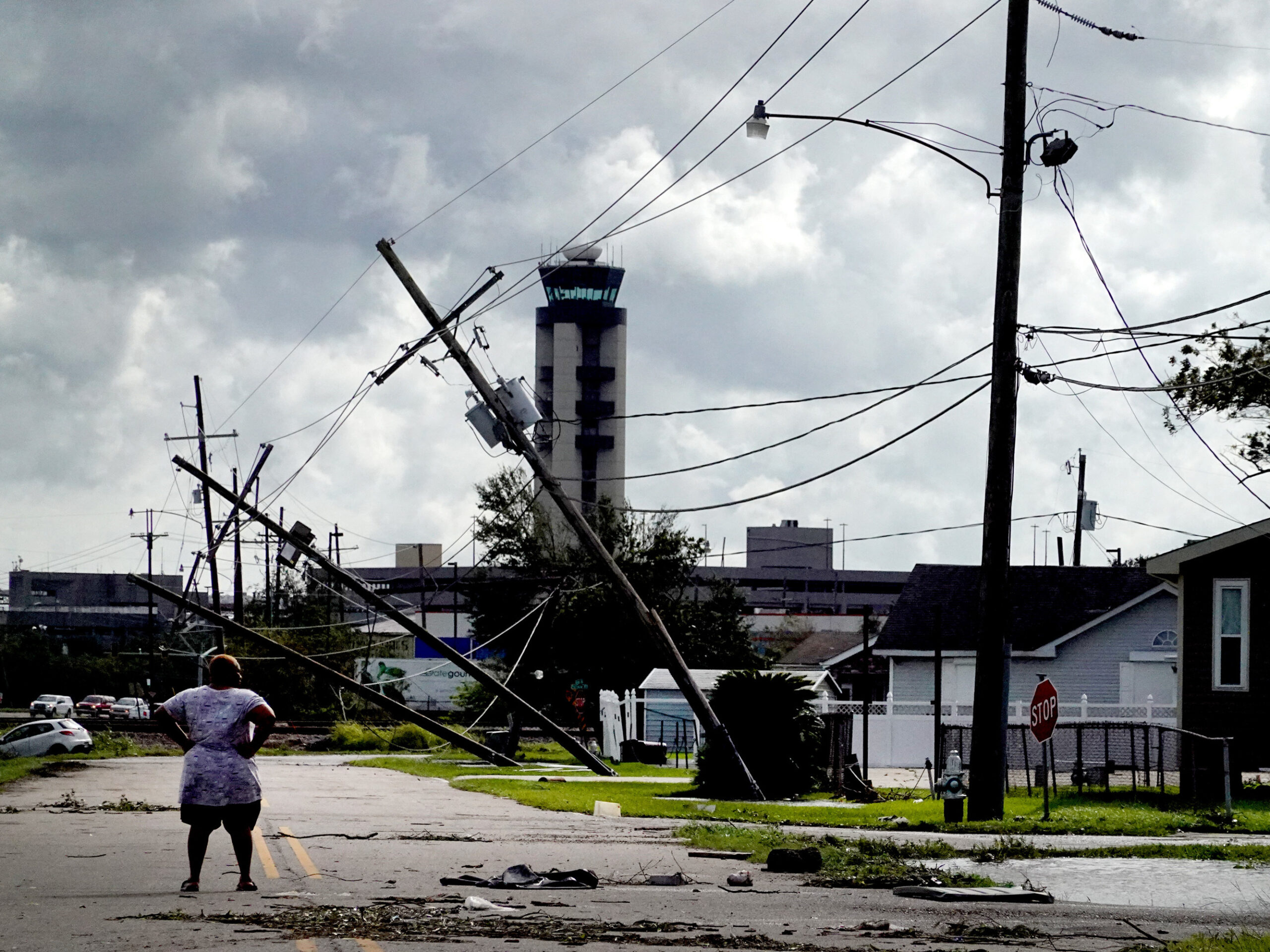 A woman stands in the middle of a street, looking at destruction, including fallen electric wires.