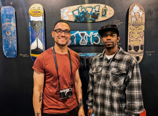 two people pose in front of painted skateboards in an art gallery