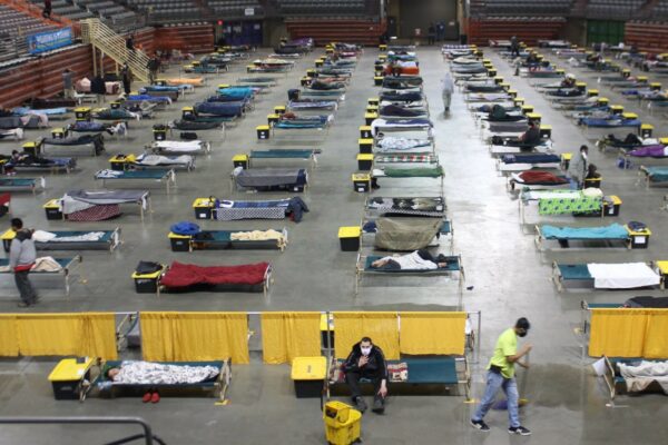 a view of the Sullivan Arena shelter floor with a number of cots and people in masks spread throughout
