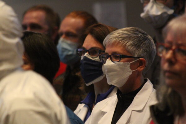 People wearing masks, some in white jackets, stare athead.