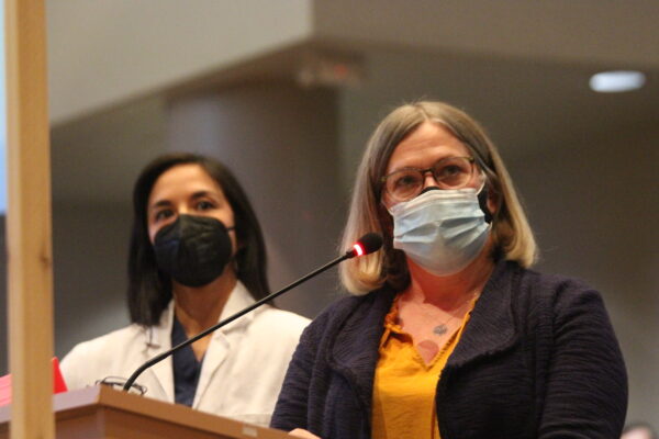 Two women in masks standing at a podium