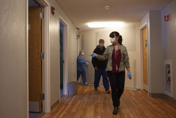 A woman wearing a mask and gloves leads two other people through a hallway.