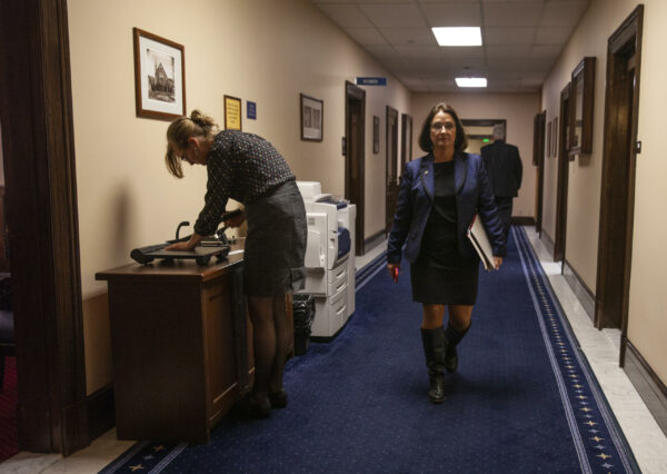A woman in a dress and boots walks down a hallway.