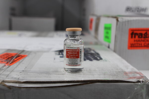 A glass vial with a clear liquid sitting on top of a cardboard box that says etesevimab injection