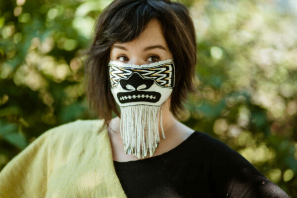 A woman with short brown hair wearing a woven mask.