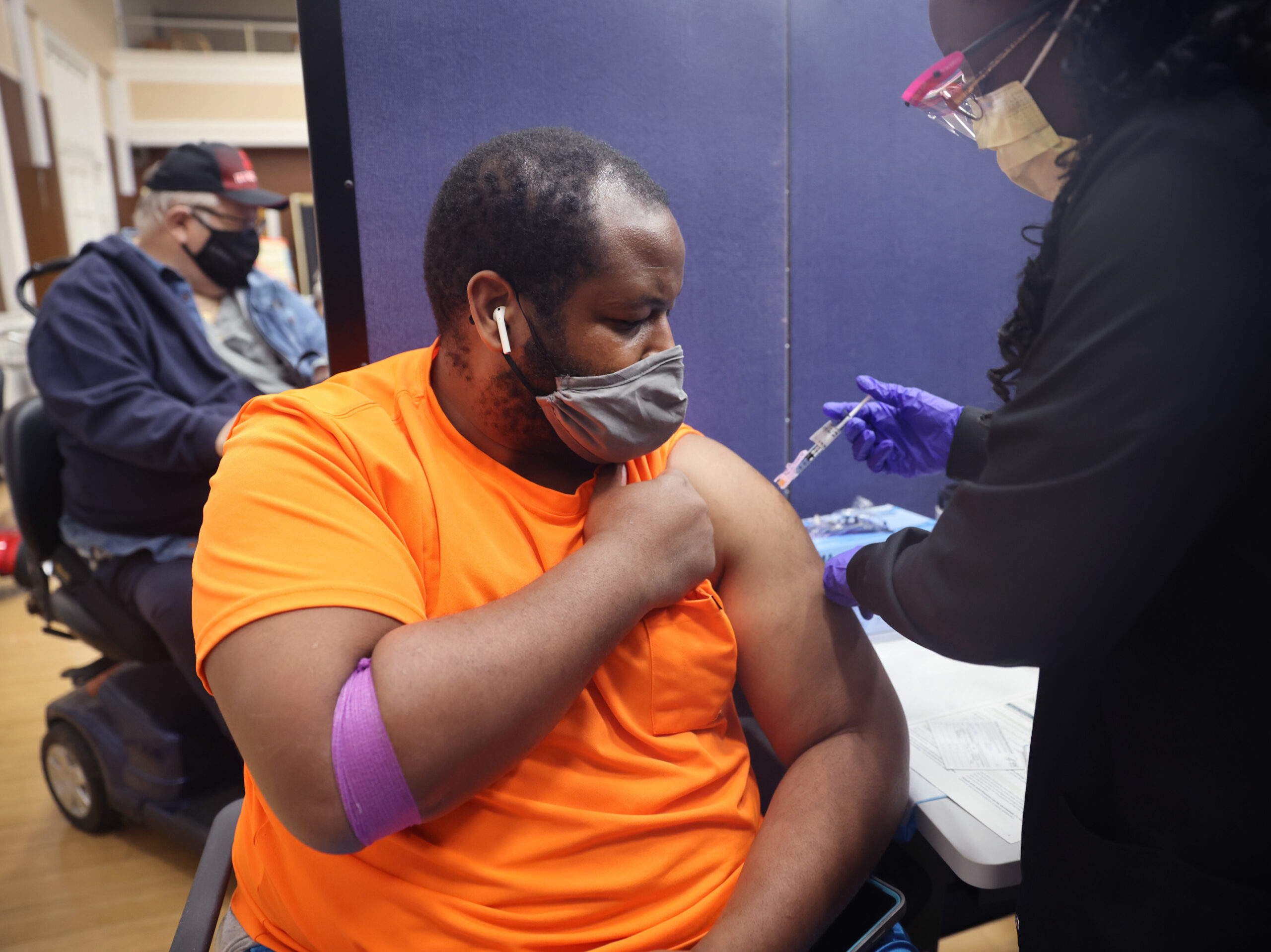 A man in an orange shirt lifts up his sleeve to get a shot.