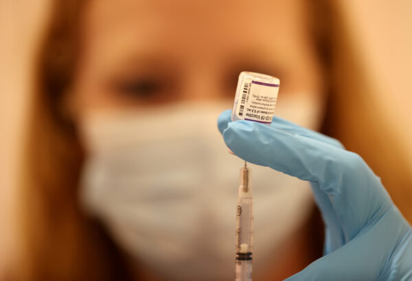 A woman in a mask gets a dose of vaccine into a needle.