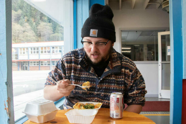 A man in a hat eats dumplings at a table indoors.