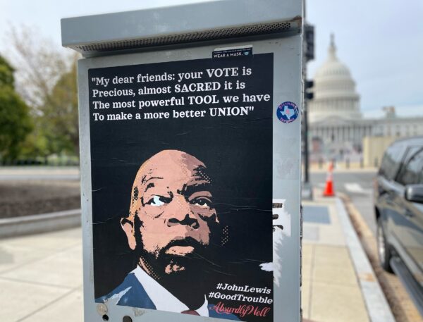 poster of John Lewis' face attached to a metal box, in front of the U.S. Capitol