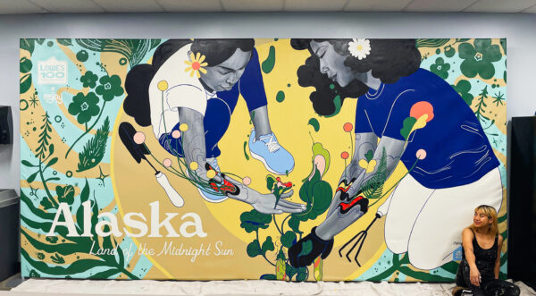 A figure sits at right in front of a colorful mural depicting two women using their hands to work with plants.