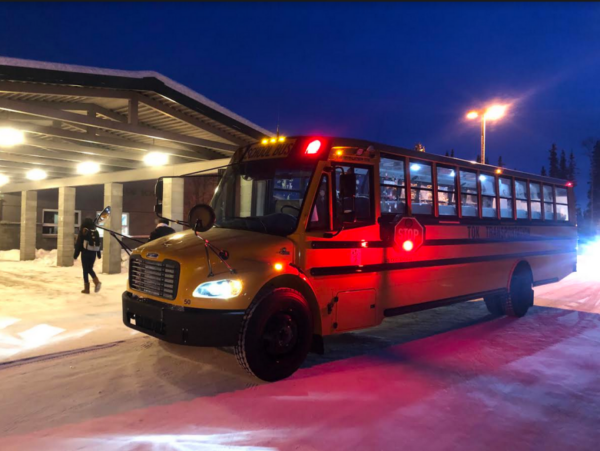 A school bus pulls up at a school in the dark.