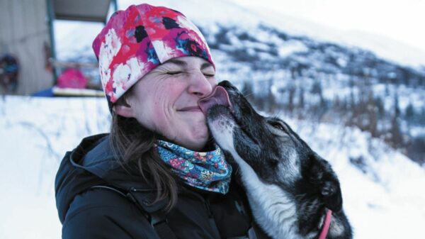A woman in a hat gets a lick on the face from a dog.