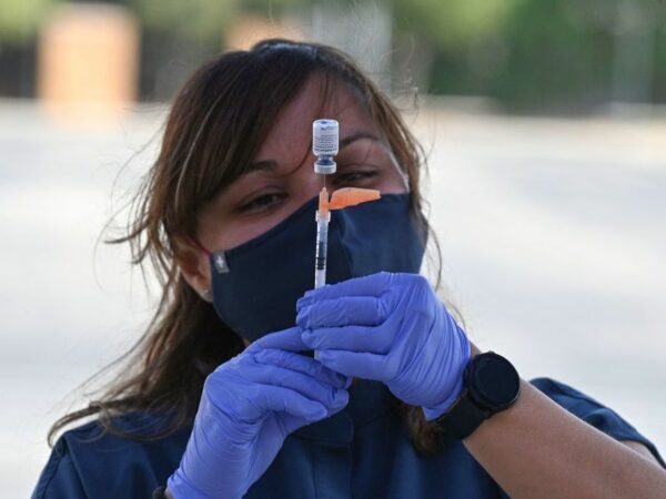A woman in purple gloves and a mask fills a shot with vaccine.