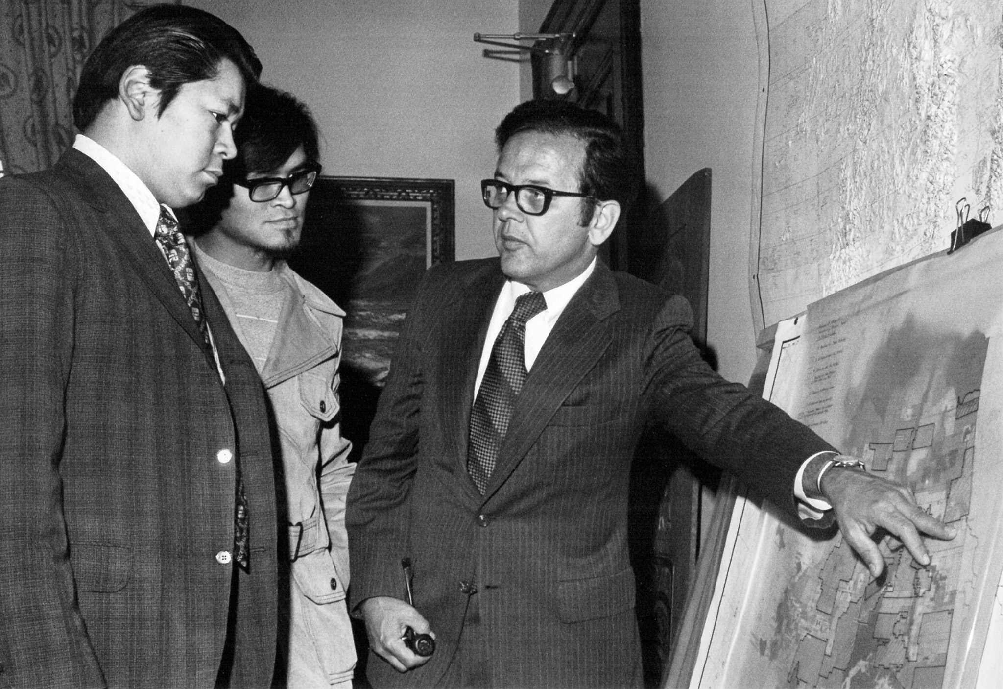 A black and white photo of a man pointing to a map.