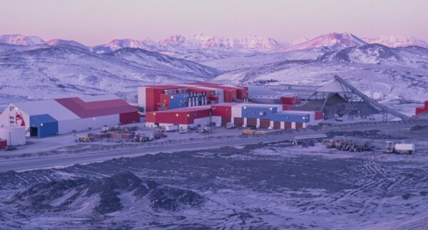 A large red hangar building with some vehicles outtside in a snowy, mountainous lanscape
