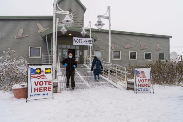 people leaving a building under a sign that says "vote here."