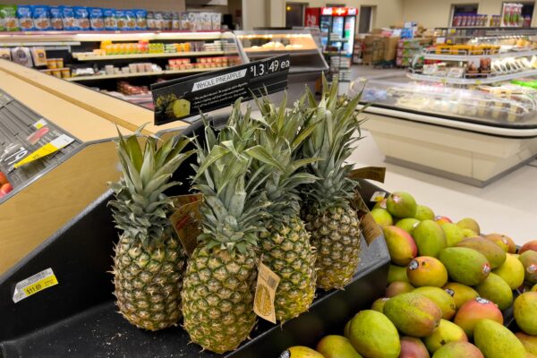 Pineapples stacked near mangos at a store.