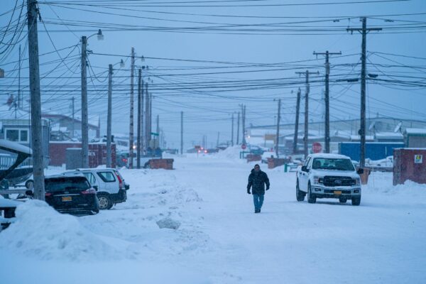 A person walks down an empty snowy street with homes on either side.