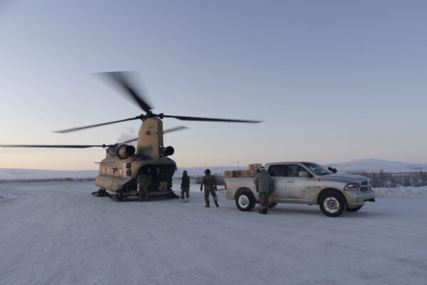 people in uniform unload gifts from a helicopter to a truck in the winter