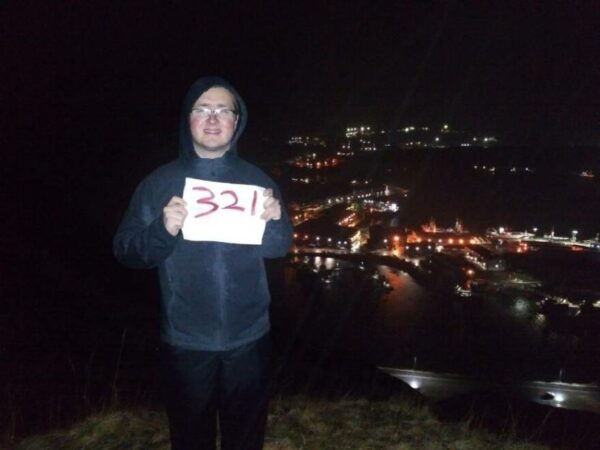 A man stands in the dark on top of a hill with a sign that says 321.