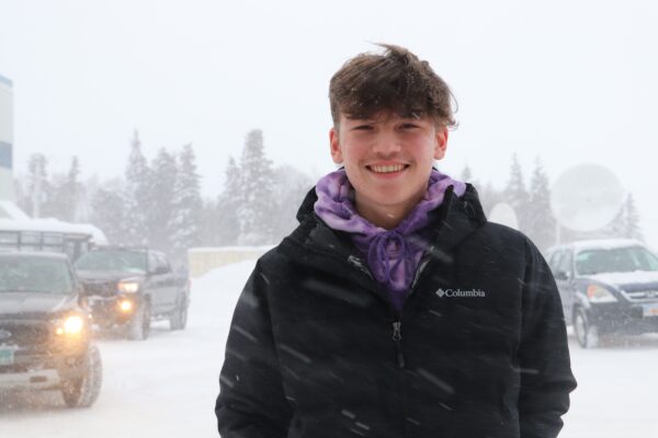 A boy in a jacket stands outside in the snow.