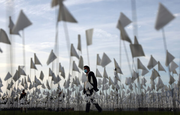A person wearing a face covering walks past a white flag memorial installation outside Griffith Observatory honoring the nearly 27,000 Los Angeles County residents who have died from COVID-19 on Nov. 18 in Los Angeles, Calif.
