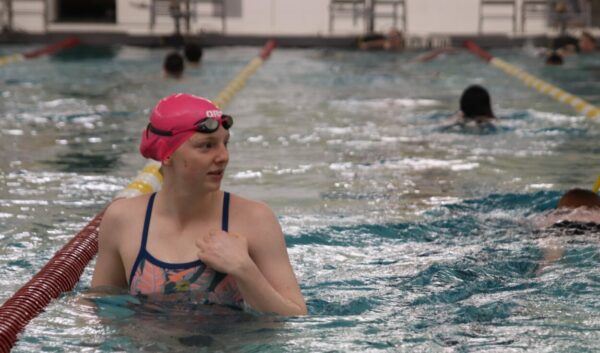 A girl in a pink swim cap looks across a lane standing in  a pool