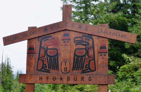 A wooden sign with stylized red and black ravens painted on it in a spruce forest