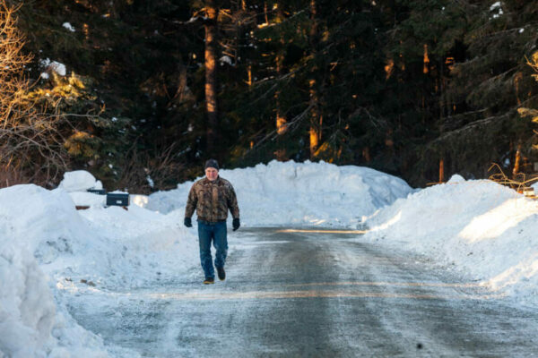 A man walks on the road with big snow berms on either side