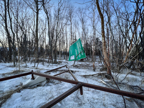 A highway sign is ripped off and laying in trees.