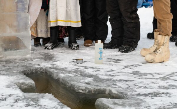 A bottle of water and a small cup sit next to a cross cut into ice.