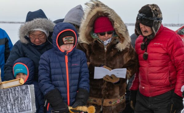 A group of people in winter clothes read a pamphlet together.