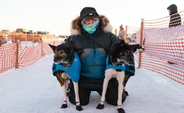 A musher poses with two sled dogs outside