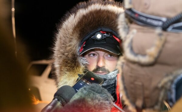 A musher talks to reporters outside
