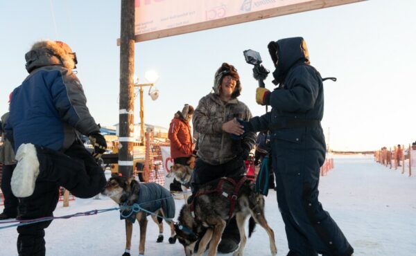 A musher shakes hands with another person near a sled dog team