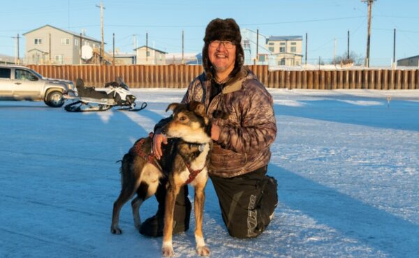 A musher poses with a sled dog outside