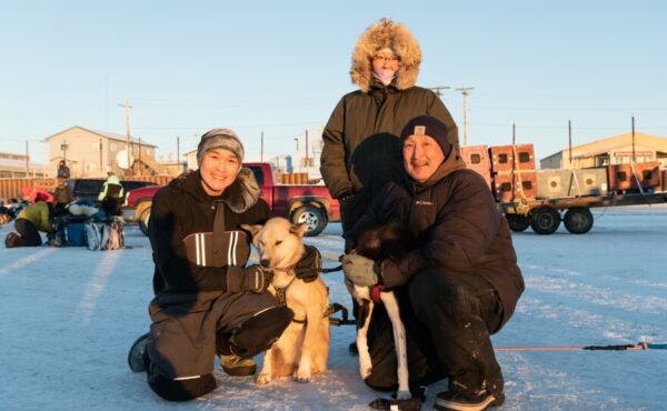A family of three post with two sled dogs