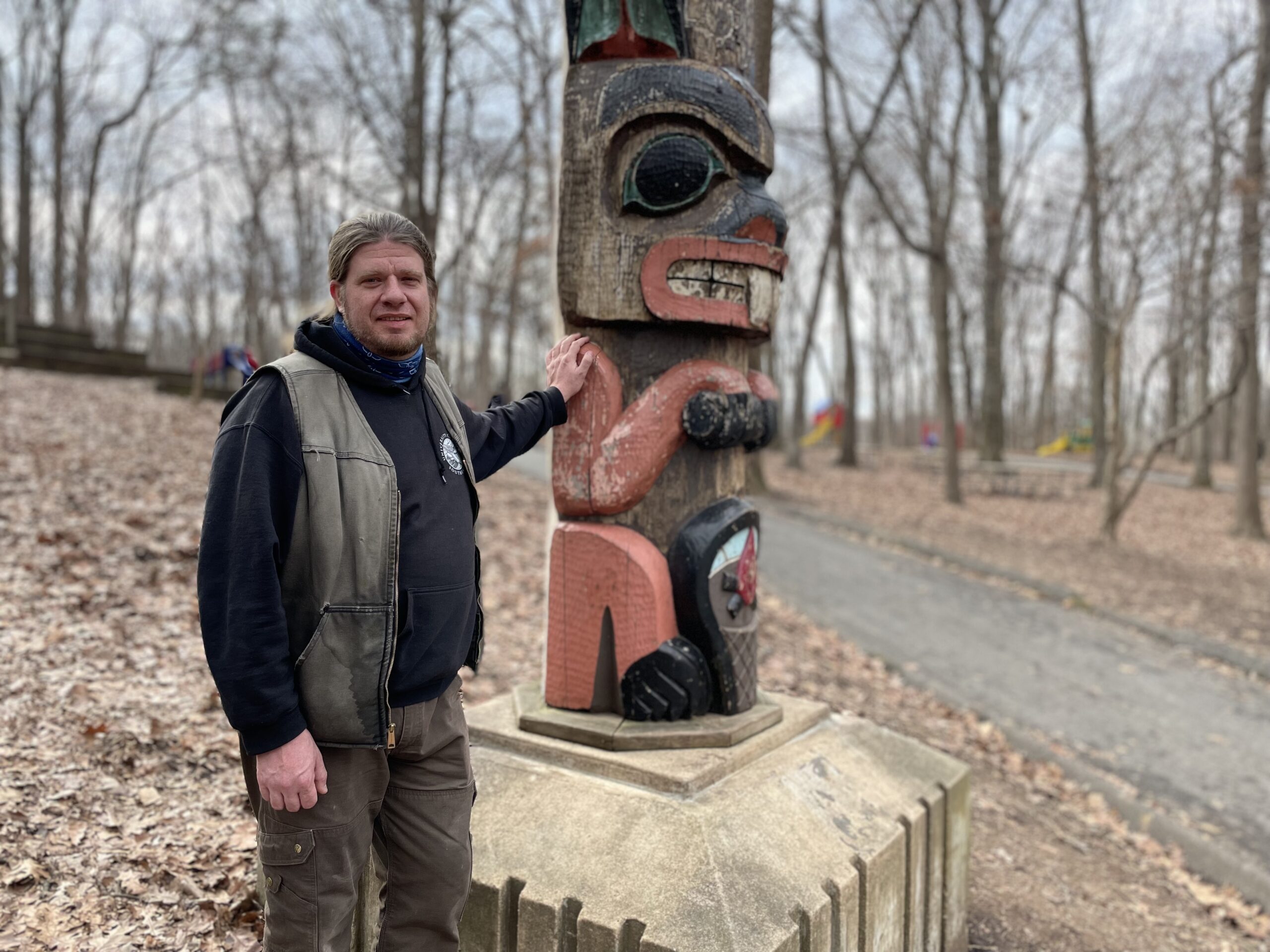 man stands by totem pole