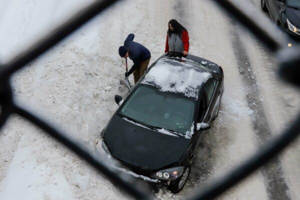 A person shovels a car out of a snowbank as another person watches.