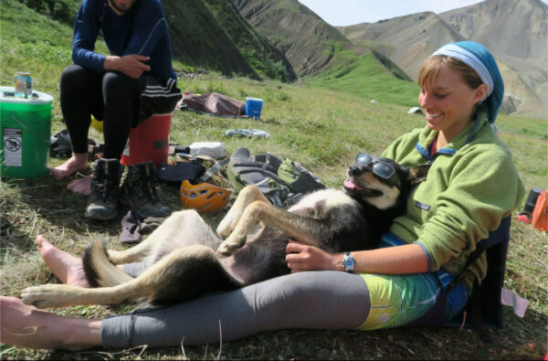 A white woman holds a dog in her lap in some green mountains