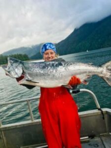 A young woman standing on the deck of a boat holding a very large king salmon