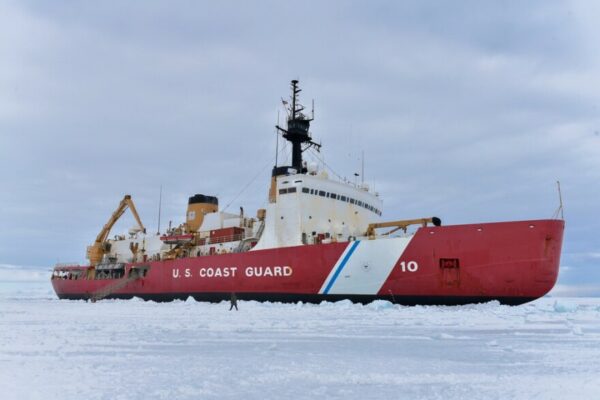 A person standing on sea ice in front of an icebreaker