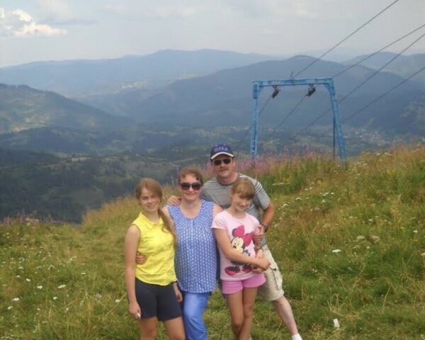 A family of four poses for a photo on top of a high hill, with mountains behind them