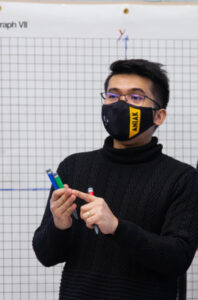 A man wearing a mask and standing at the front of a classroom