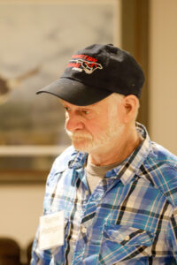 A portrait of a man in a plaid shirt and a "Redington" baseball cap