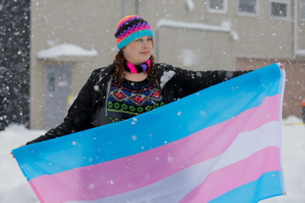 A woman holding a blue and pink striped flag in a snow storm
